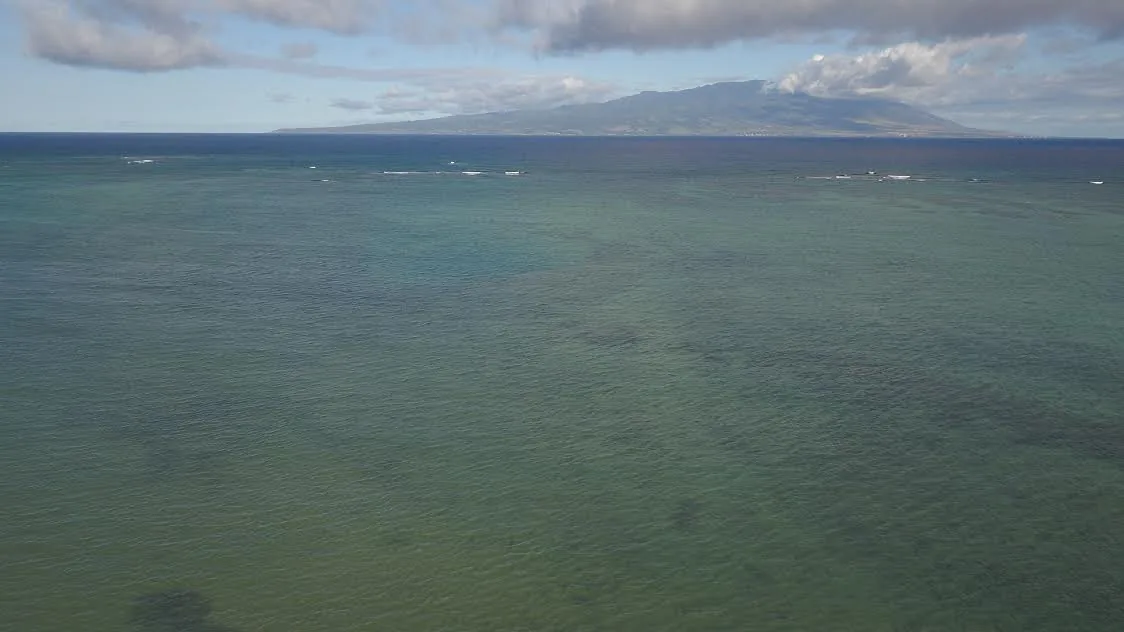 Calm reef-flat waters off Molokaʻi’s south shore with a neighbor island on the horizon